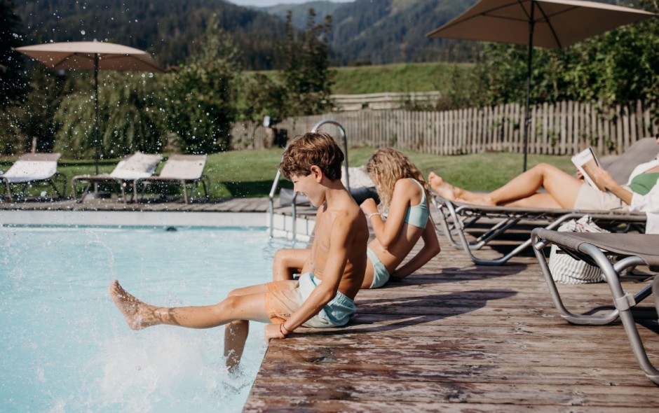 Eltern entspannen auf Liegestühlen am Pool, Kinder spielen im Pool vom Hotel Resl