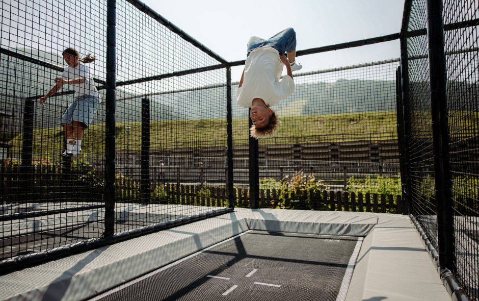 Kinder springen auf einer gesicherten Outdoor-Trampolinanlage im Familienhotel mit Bergpanorama